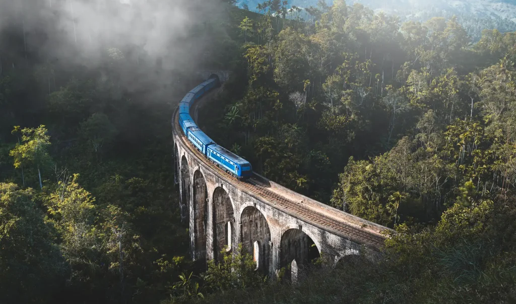 The iconic blue train crossing the Nine Arches Bridge in Ella's lush jungle, a highlight of our Sri Lanka holiday packages.