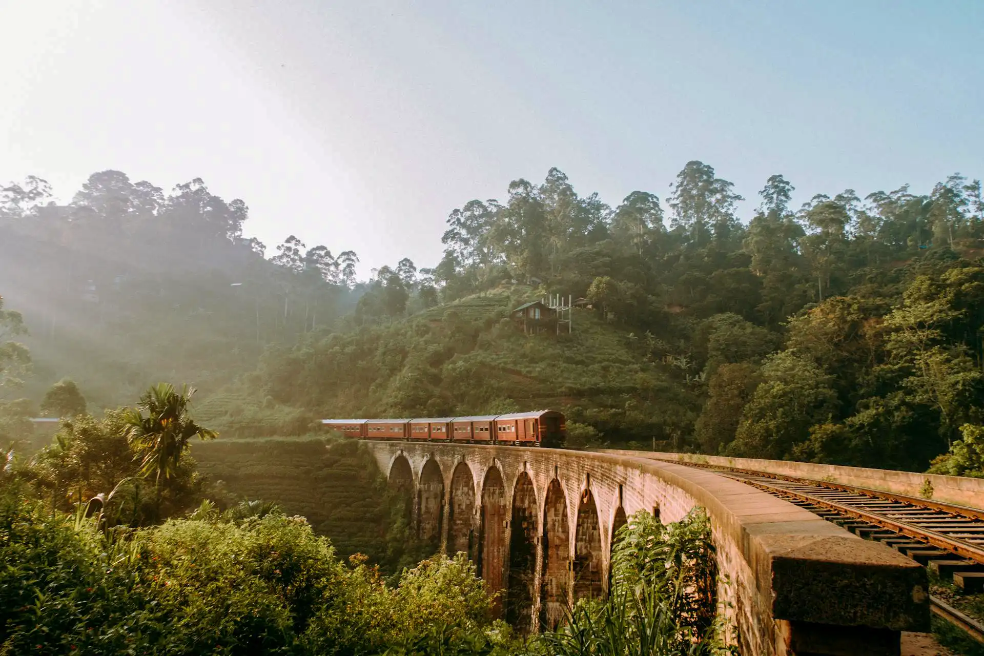 A vintage red train crossing the spectacular Nine Arches Bridge in Ella, a scenic mountain highlight on our ella to galle 5 day tour package