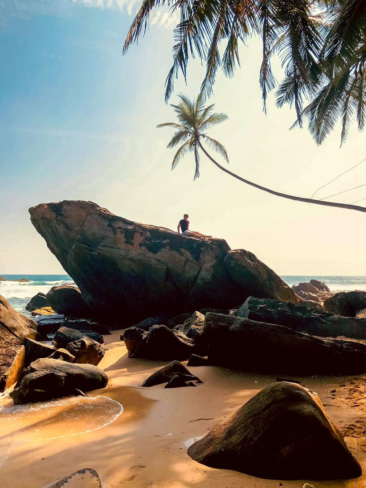 Relaxing on a large rock under a leaning palm tree at Unawatuna Beach, a beautiful coastal stop on your 1 week sri lanka complete discovery tour